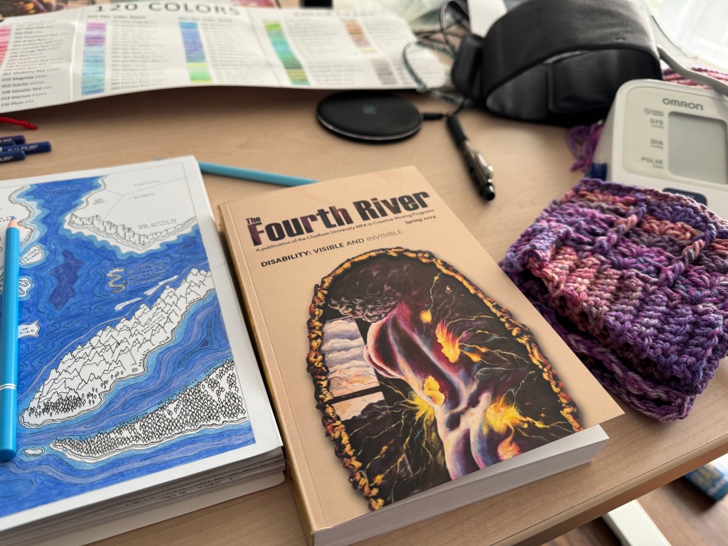 A desk that has several things on it-a coloring page of a depth map of the ocean, a purple knit hand warmer, a blood pressure cuff, the book The Fourth River. The cover is beige with a piece of purplish artwork showing lighting and flames coming into or out of someone's bare back.